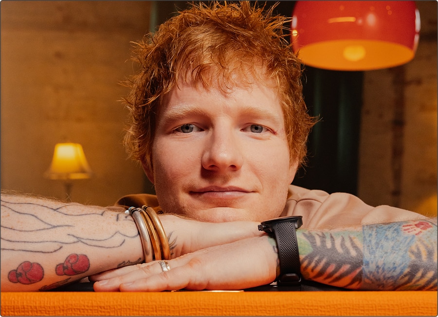 Ed Sheeran resting his arms on an Orange amplifier.
