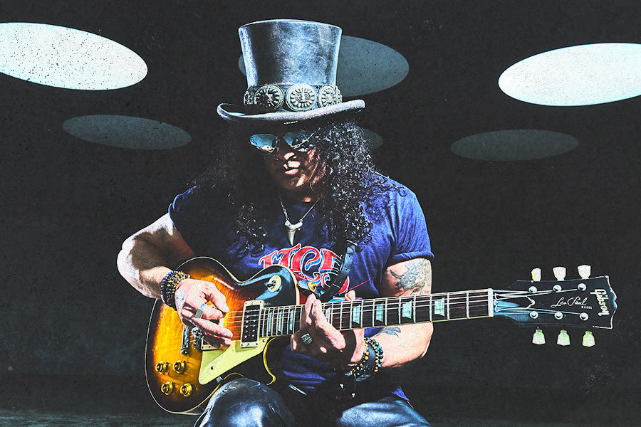 Slash seated with a Les Paul guitar under stage lights.